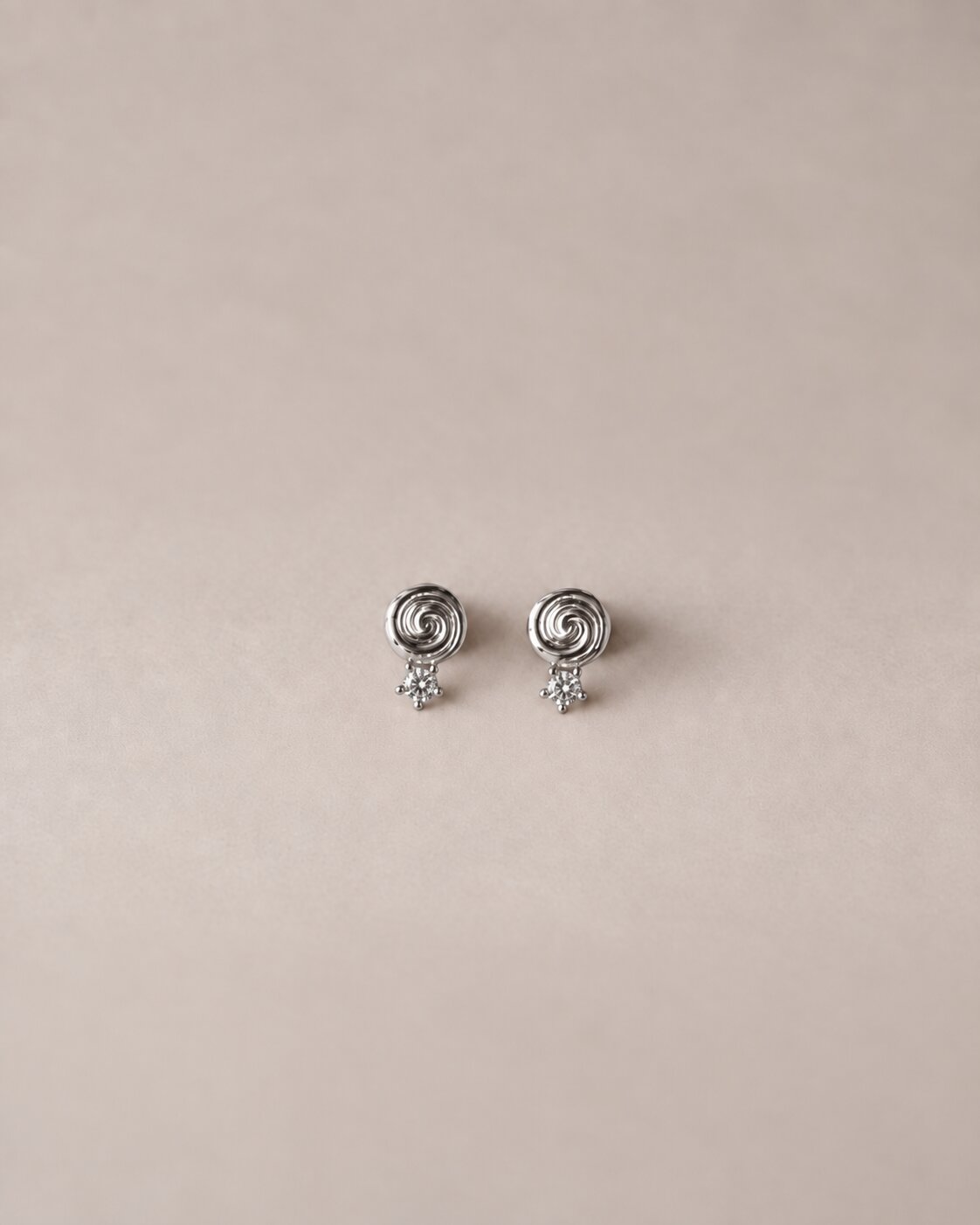 A pair of silver stud earrings, each featuring a small spiral top with a tiny dangling star, displayed on a solid beige background.