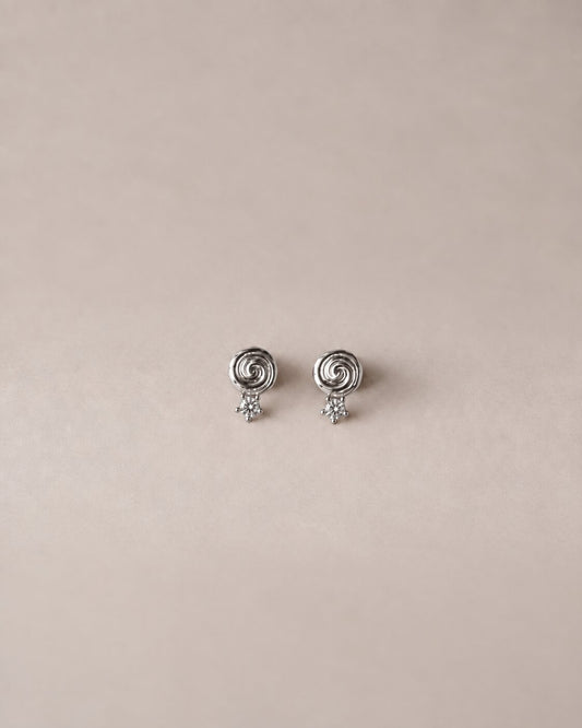 A pair of silver stud earrings, each featuring a small spiral top with a tiny dangling star, displayed on a solid beige background.