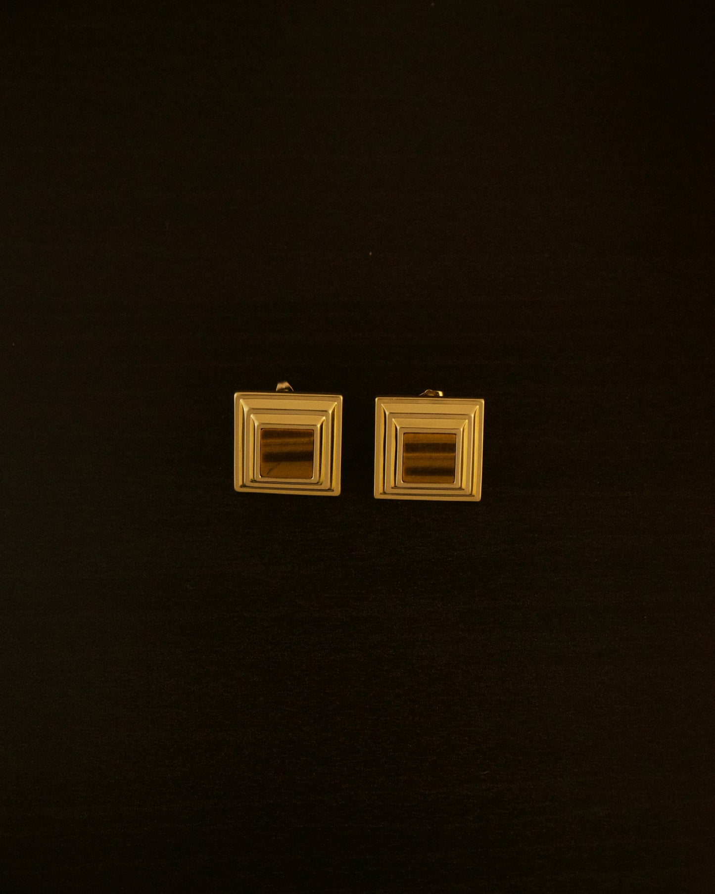 LEO earrings – close-up of 18k gold sculptural earrings with a yellow tiger eye stone centered in a bold, curved design.