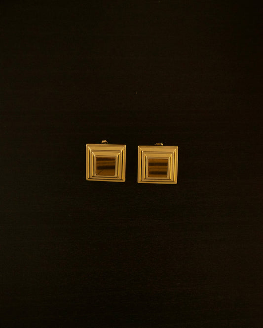 LEO earrings – close-up of 18k gold sculptural earrings with a yellow tiger eye stone centered in a bold, curved design.