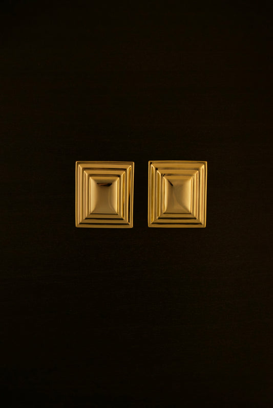 SIENTA gold earrings – close-up of rectangular sculptural earrings in polished gold, with a sleek, elongated design.