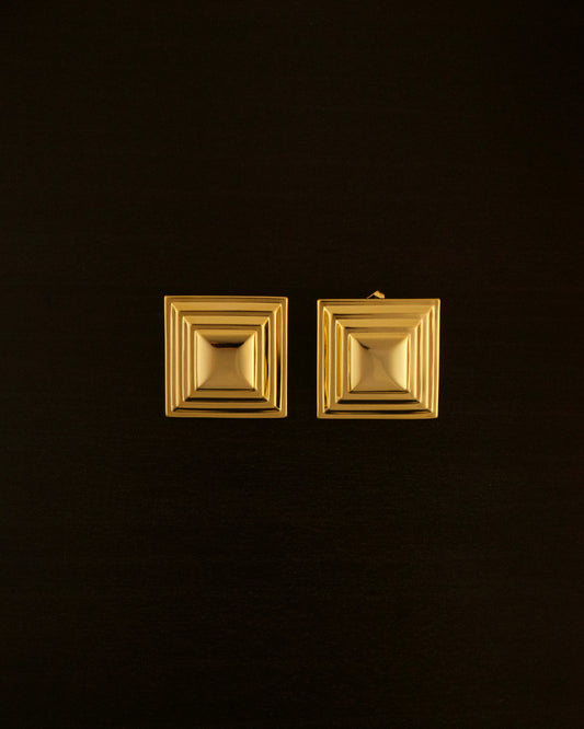SIENTE gold earrings – close-up of square sculptural earrings in polished gold with a bold, minimalist design.