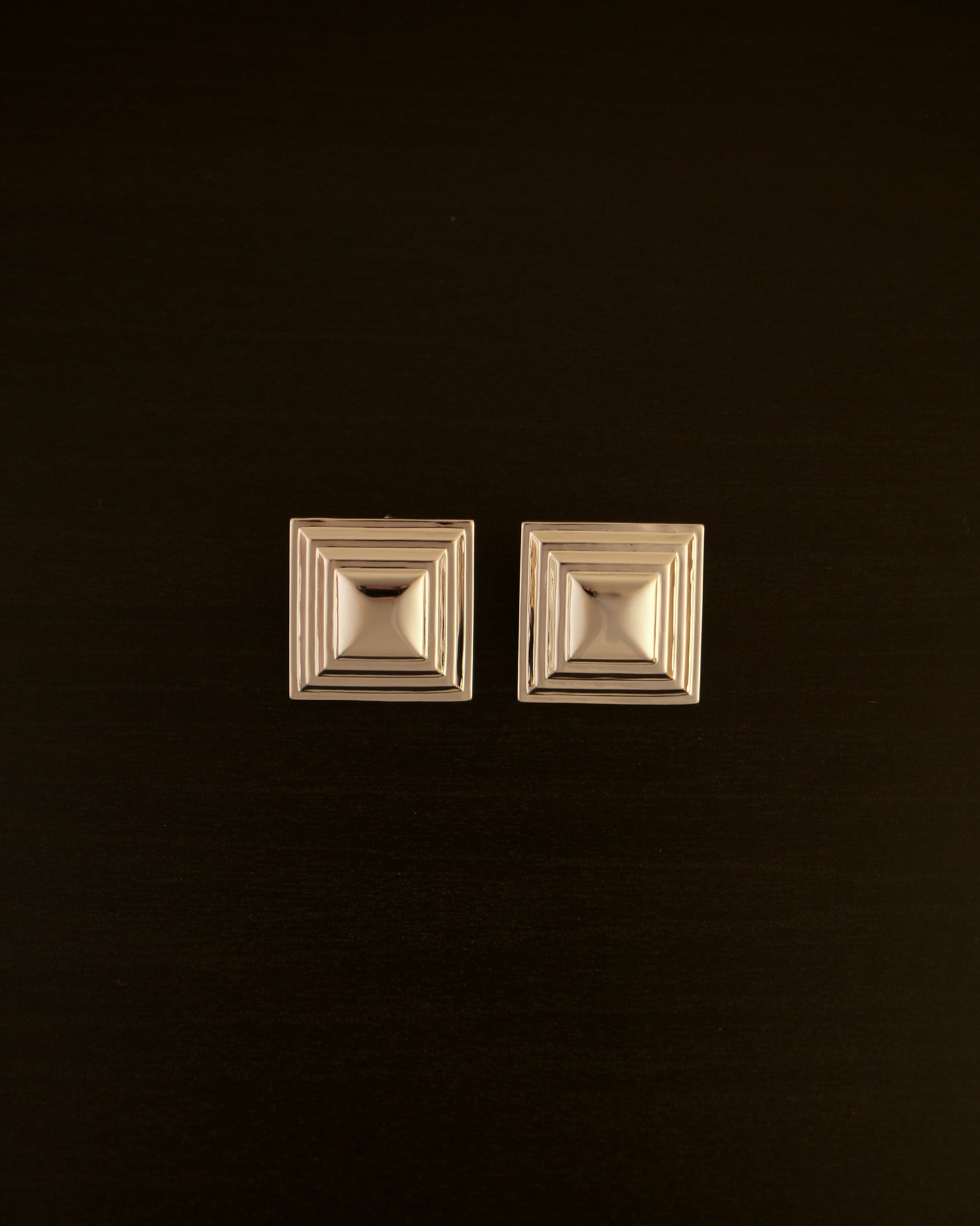 SIENTE gold earrings – close-up of square sculptural earrings in polished gold with a bold, minimalist design.