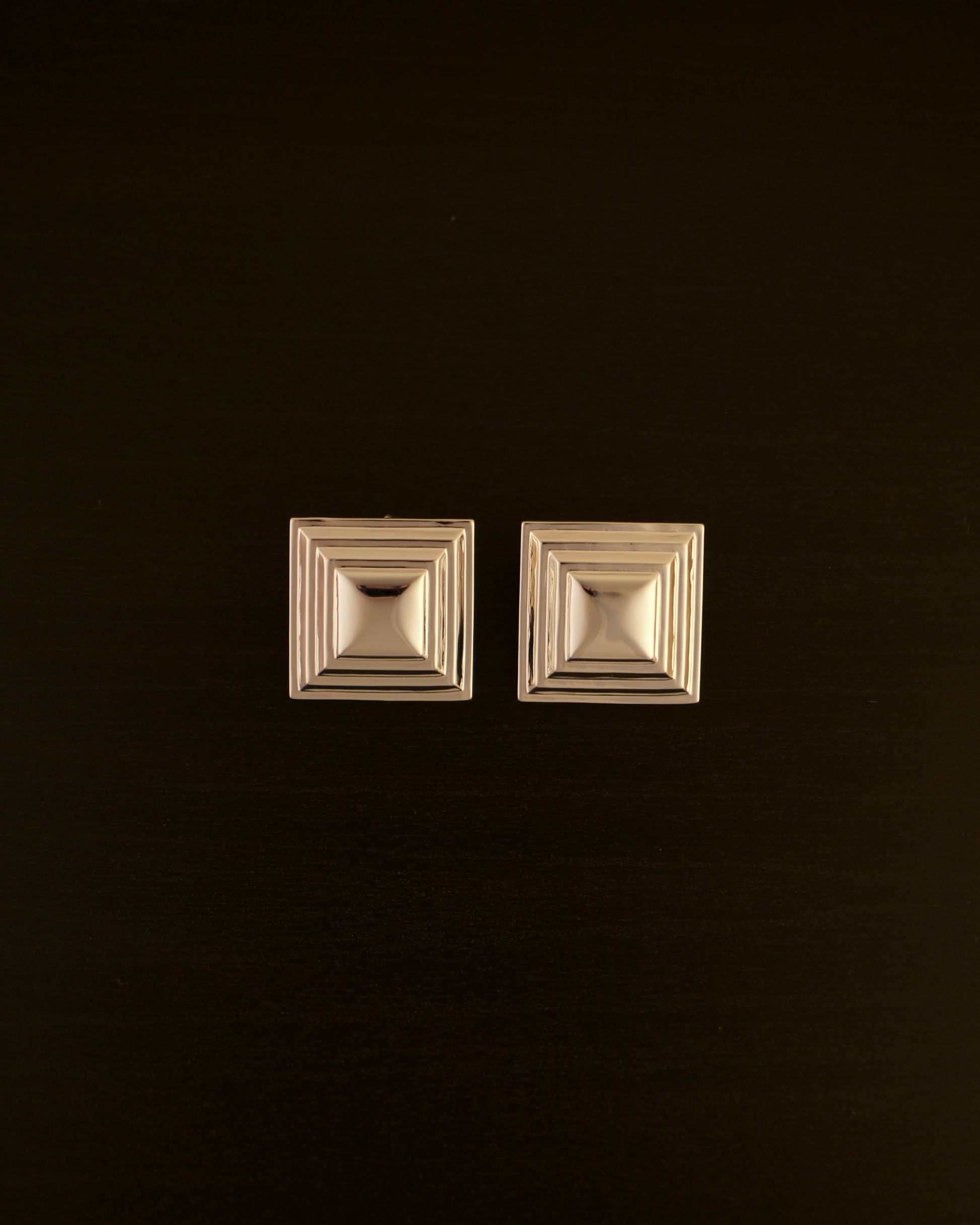SIENTE gold earrings – close-up of square sculptural earrings in polished gold with a bold, minimalist design.
