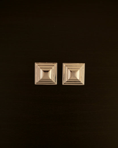 SIENTE gold earrings – close-up of square sculptural earrings in polished gold with a bold, minimalist design.