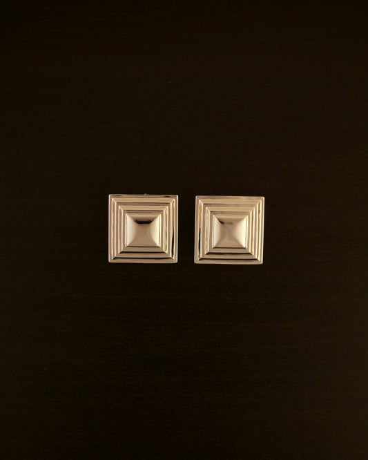 SIENTE gold earrings – close-up of square sculptural earrings in polished gold with a bold, minimalist design.