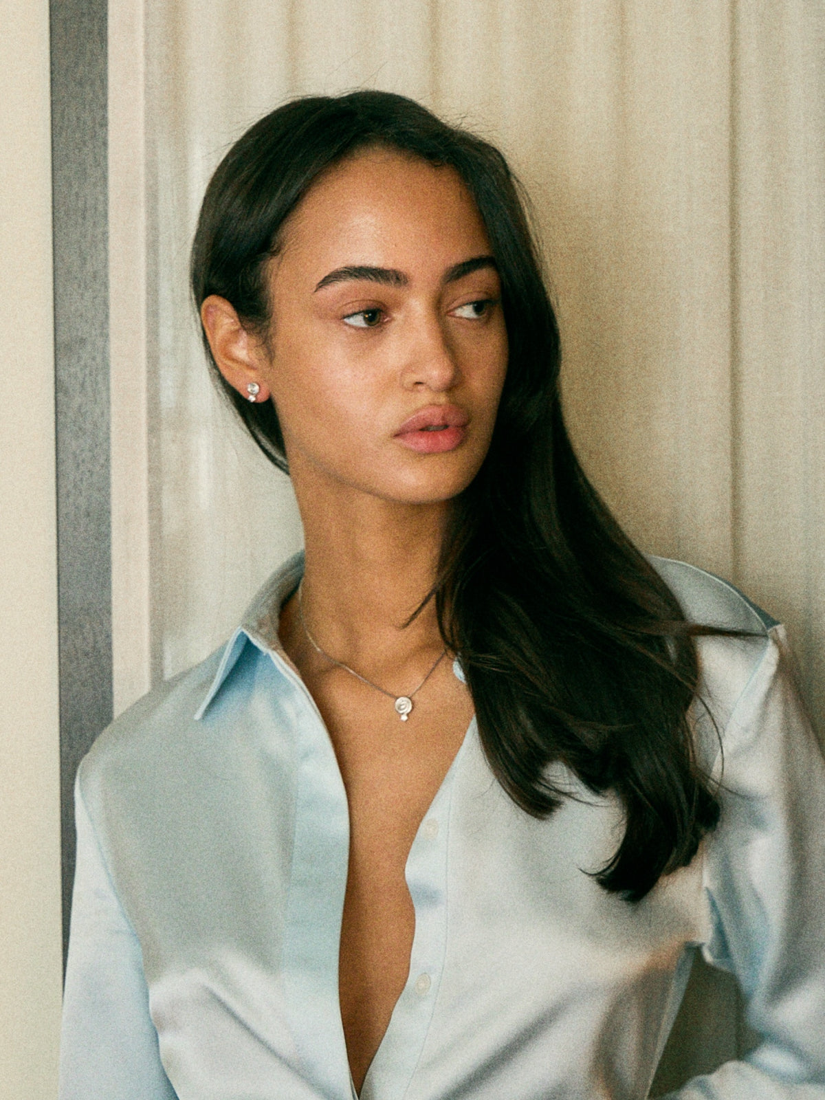 Model in a blue silk shirt wearing Cold Edges Alba gold spiral pendant necklace and spiral stud earrings