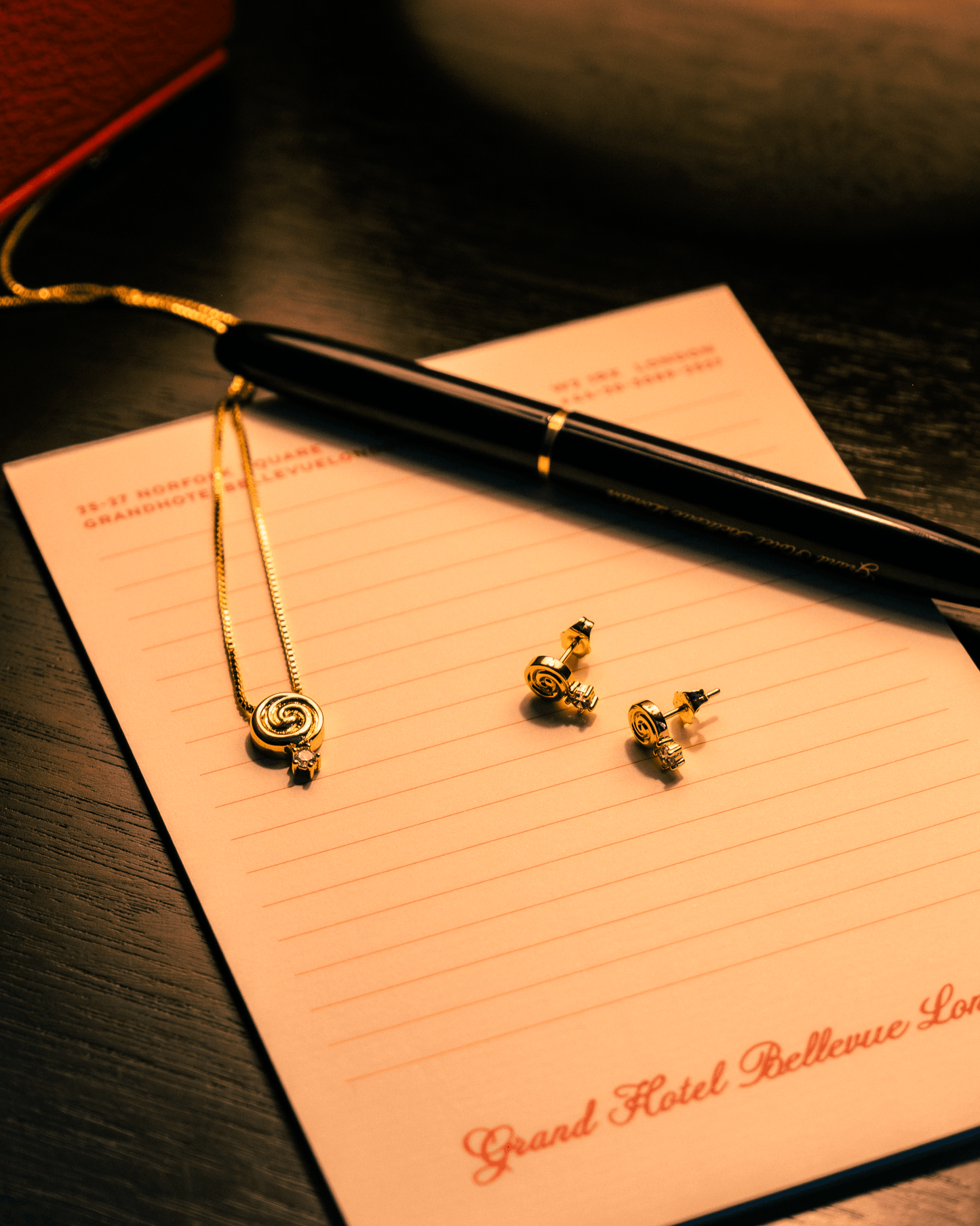 Cold Edges Alba gold spiral pendant necklace and matching spiral stud earrings styled on a hotel notepad