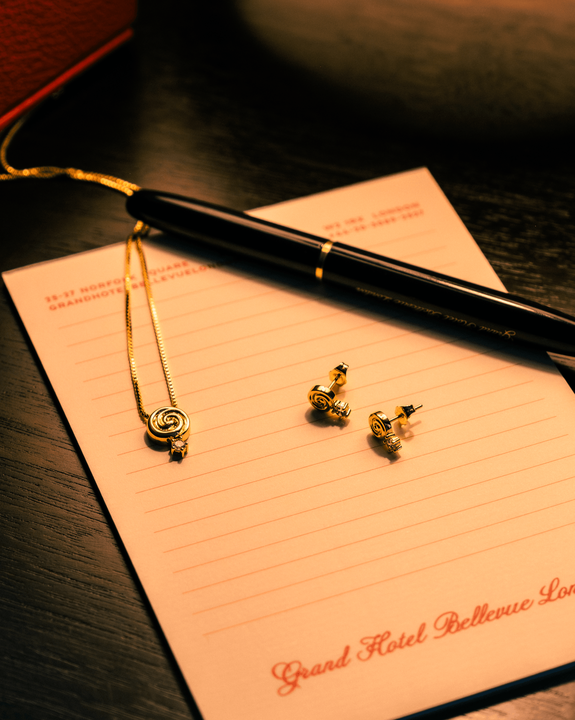 Cold Edges Alba gold spiral pendant necklace and matching spiral stud earrings styled on a hotel notepad